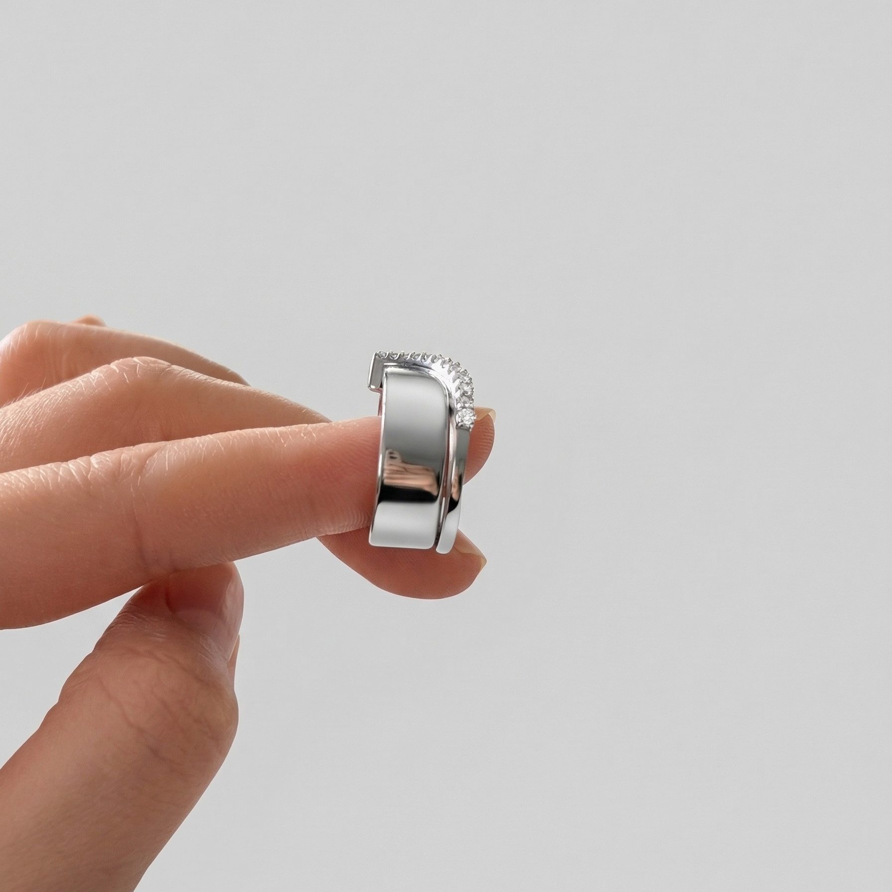 Silver ring held between fingers against a plain background